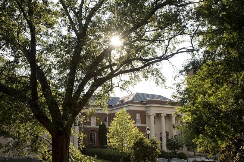 The front entrance of Brooks Hall with the summer afternoon sun filtering through the trees.