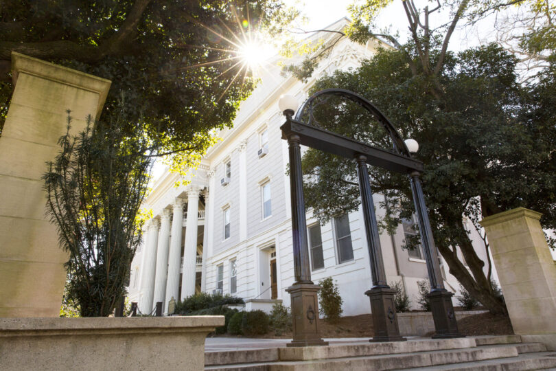 The Arch with the Holmes-Hunter Academic Building in the background as the sun peeks through the overhanging trees.