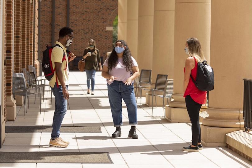 (L-R) Undergraduates Caleb Kelly, Stephania Luna, and Darby Day socialize while wearing face coverings maintaining social distancing on the balcony of Amos Hall at the Terry Business Learning Community.